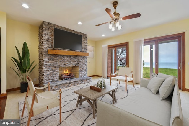 living room featuring light wood-type flooring, a fireplace, ceiling fan, and a water view