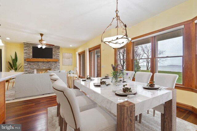 dining space featuring ceiling fan with notable chandelier, dark hardwood / wood-style floors, and a fireplace