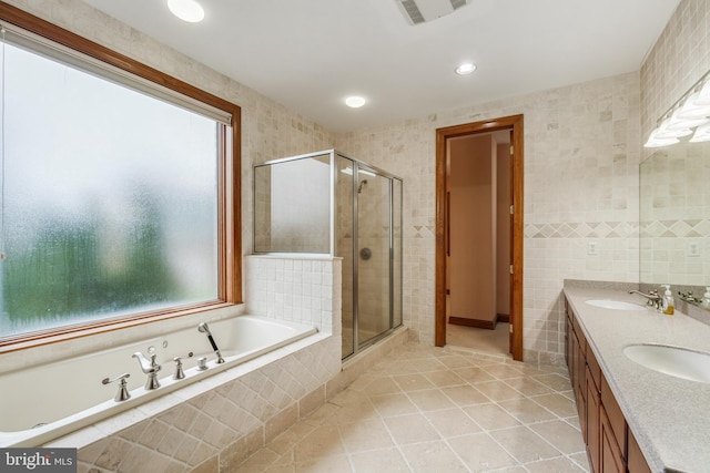 bathroom featuring tile walls, tile floors, independent shower and bath, and dual bowl vanity