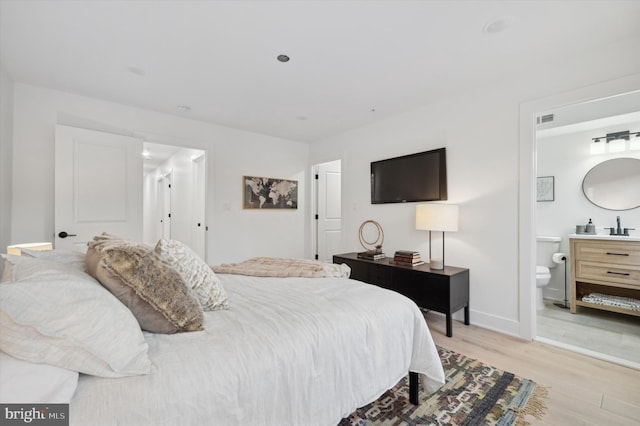 bedroom with ensuite bath, sink, and light hardwood / wood-style flooring