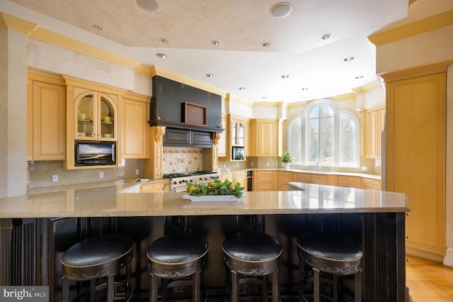 kitchen with gas stove, a kitchen bar, light brown cabinetry, custom exhaust hood, and backsplash