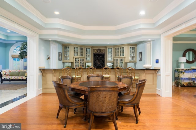 dining area featuring bar area, crown molding, a raised ceiling, and light hardwood / wood-style flooring