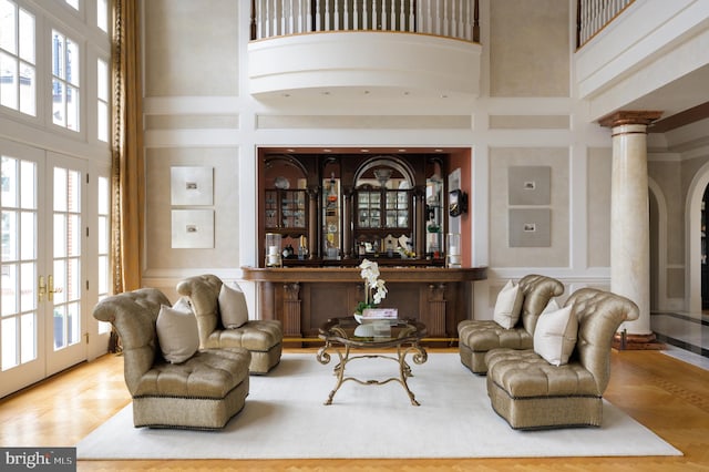 living room featuring french doors, a wealth of natural light, ornate columns, and a towering ceiling