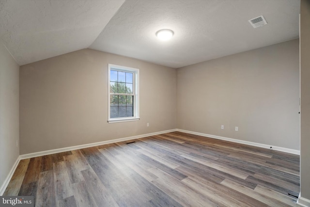 empty room with a textured ceiling, wood-type flooring, and vaulted ceiling