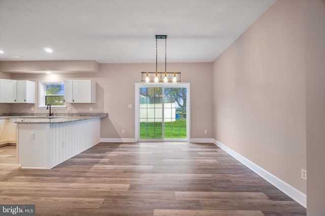 kitchen with kitchen peninsula, hanging light fixtures, white cabinets, light hardwood / wood-style floors, and a notable chandelier