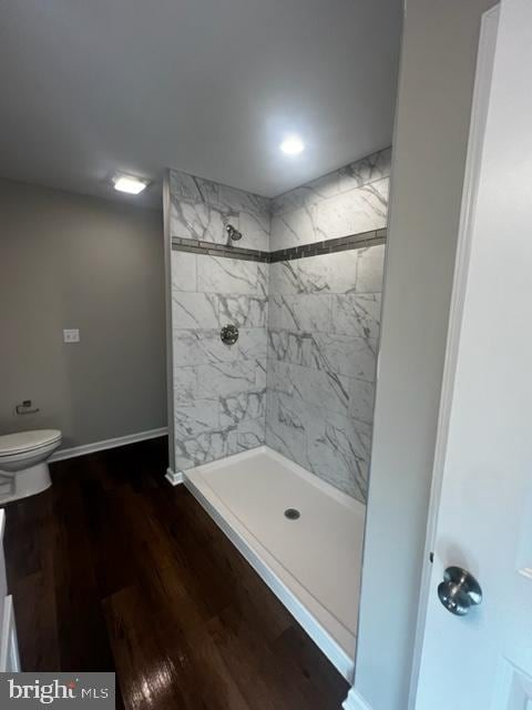 bathroom with a tile shower, hardwood / wood-style flooring, and toilet