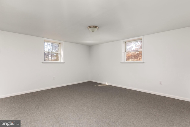 empty room featuring plenty of natural light and dark colored carpet