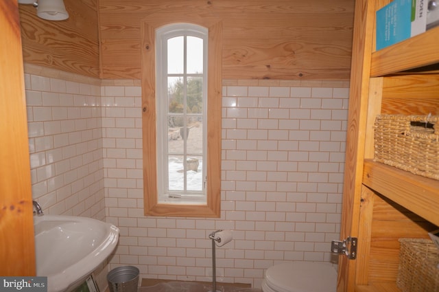 bathroom with tile walls, toilet, wooden walls, and sink