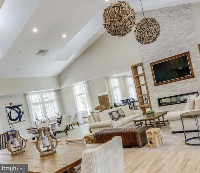 living room with a stone fireplace, high vaulted ceiling, and light hardwood / wood-style floors