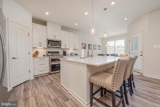 kitchen with hardwood / wood-style floors, hanging light fixtures, a center island with sink, stainless steel appliances, and white cabinetry