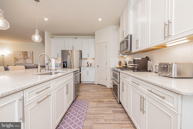 kitchen featuring decorative light fixtures, appliances with stainless steel finishes, sink, light wood-type flooring, and white cabinets