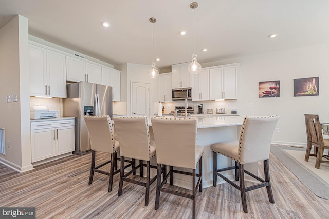 kitchen featuring light wood-type flooring, a breakfast bar, stainless steel appliances, decorative light fixtures, and white cabinetry