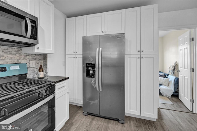 kitchen with backsplash, light wood-type flooring, appliances with stainless steel finishes, and white cabinetry