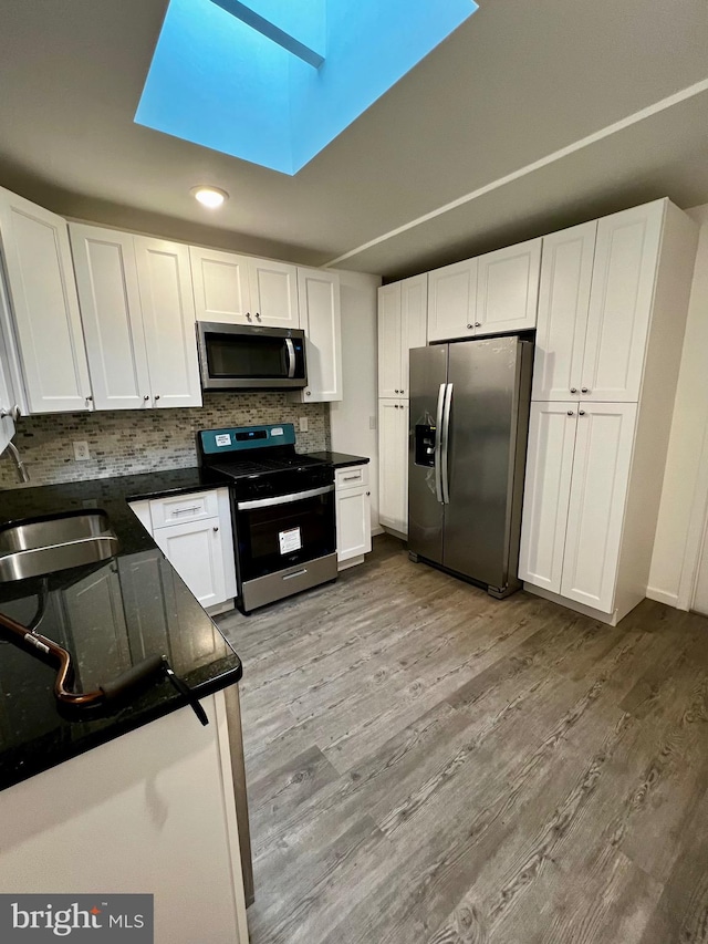 kitchen with appliances with stainless steel finishes, light hardwood / wood-style floors, white cabinets, backsplash, and sink