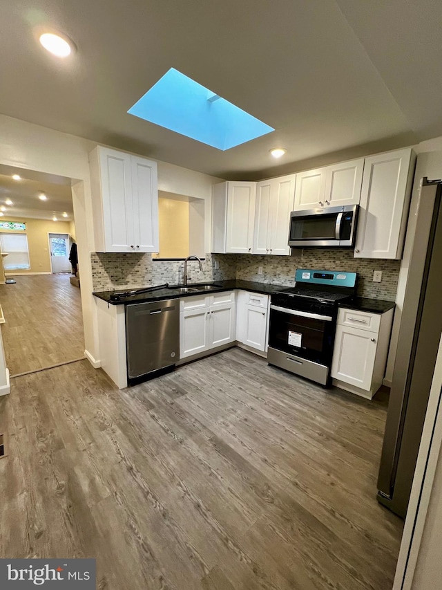 kitchen with white cabinets, a skylight, stainless steel appliances, and light hardwood / wood-style flooring