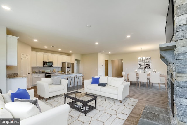 living room with light hardwood / wood-style flooring, a stone fireplace, and an inviting chandelier