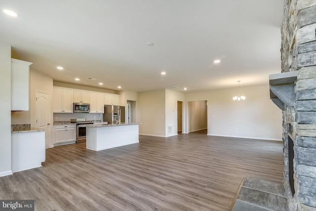 kitchen with a chandelier, white cabinetry, an island with sink, stainless steel appliances, and hardwood / wood-style floors