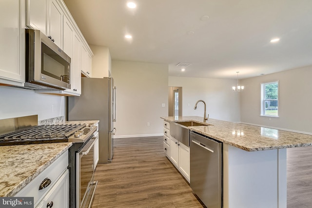 kitchen with a notable chandelier, appliances with stainless steel finishes, a center island with sink, and light hardwood / wood-style flooring