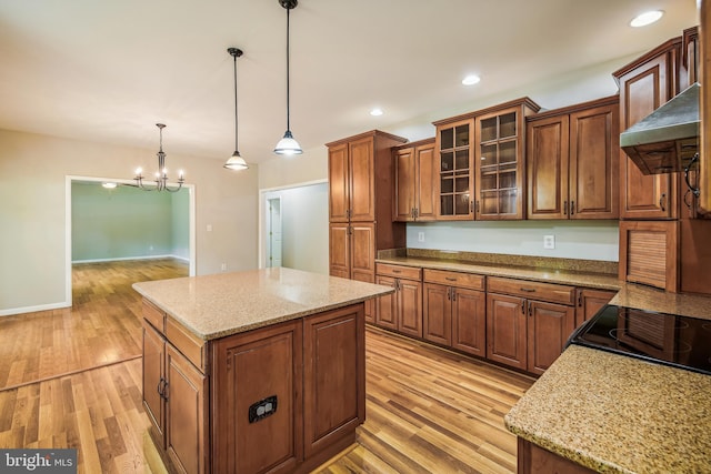 kitchen featuring light stone counters, a center island, hanging light fixtures, and light hardwood / wood-style flooring