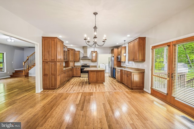 kitchen with wall chimney exhaust hood, light wood-type flooring, decorative light fixtures, a kitchen island, and stainless steel appliances