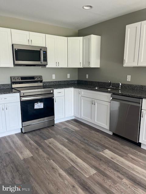 kitchen featuring dark stone countertops, white cabinetry, dark hardwood / wood-style flooring, sink, and appliances with stainless steel finishes