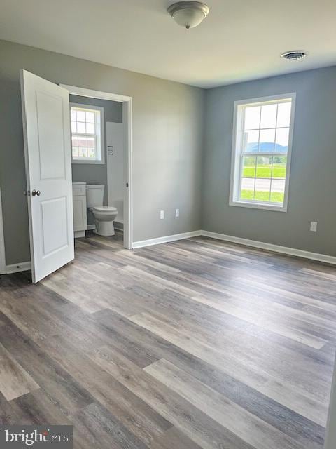 unfurnished bedroom featuring hardwood / wood-style floors, ensuite bathroom, and multiple windows