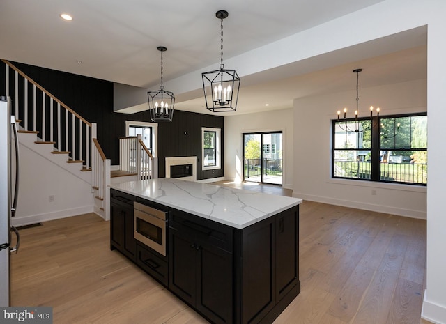 kitchen with an inviting chandelier, stainless steel microwave, light hardwood / wood-style flooring, and pendant lighting