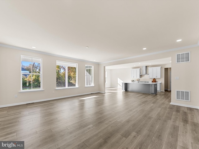 unfurnished living room with light wood-type flooring, ornamental molding, and sink