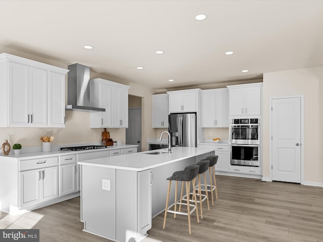 kitchen featuring appliances with stainless steel finishes, white cabinetry, wall chimney exhaust hood, and sink