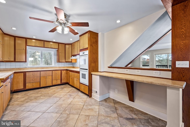 kitchen with light tile flooring, white double oven, ceiling fan, tasteful backsplash, and built in desk