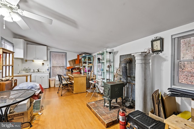 interior space featuring a wood stove, ceiling fan, light wood-type flooring, sink, and lofted ceiling