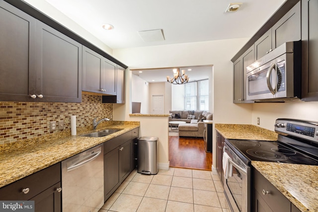 kitchen with stainless steel appliances, light tile floors, sink, a chandelier, and light stone countertops