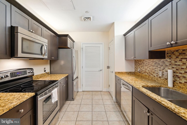 kitchen with appliances with stainless steel finishes, backsplash, light tile floors, sink, and light stone countertops