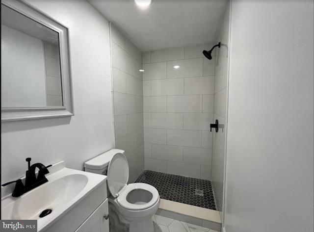 bathroom with toilet, a tile shower, large vanity, and tile flooring