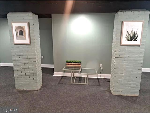 basement featuring brick wall and dark colored carpet