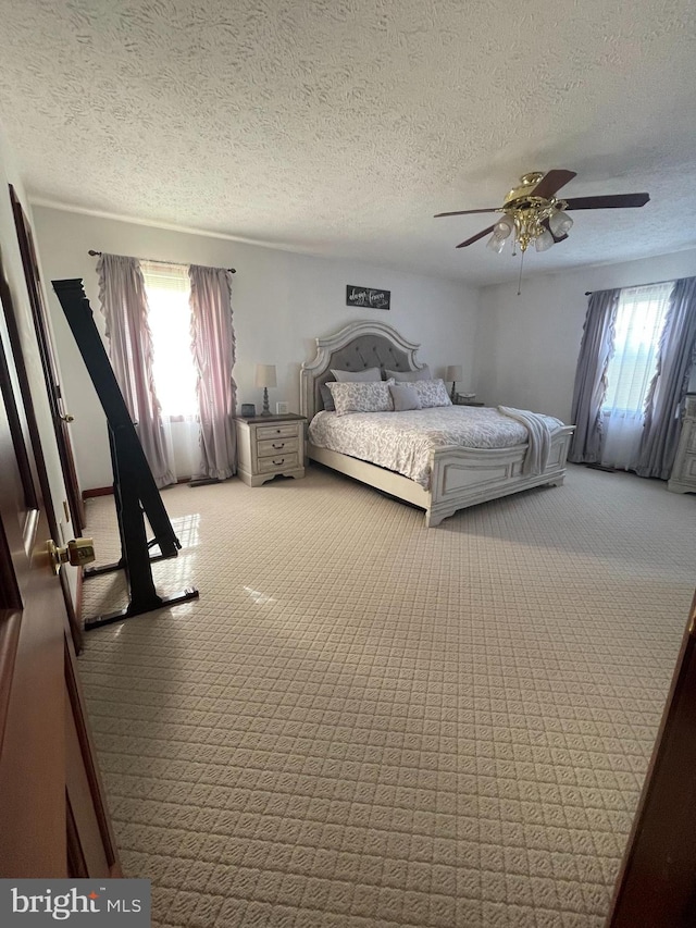 unfurnished bedroom with light colored carpet, ceiling fan, multiple windows, and a textured ceiling