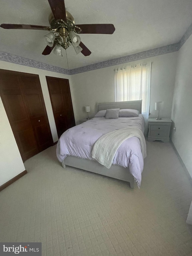 bedroom with light carpet, ceiling fan, and two closets