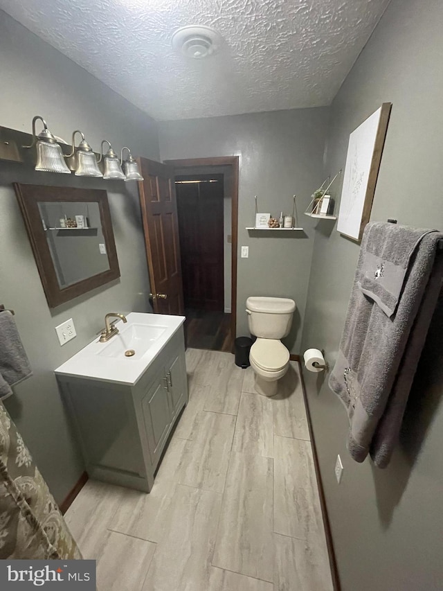 bathroom featuring vanity, a textured ceiling, hardwood / wood-style floors, and toilet