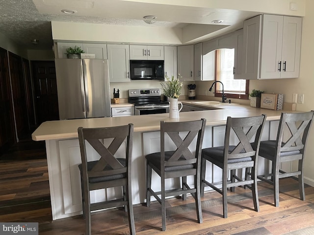 kitchen with stainless steel appliances, a kitchen bar, dark hardwood / wood-style flooring, sink, and gray cabinets