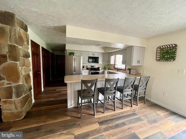 kitchen featuring kitchen peninsula, dark hardwood / wood-style floors, appliances with stainless steel finishes, sink, and a textured ceiling