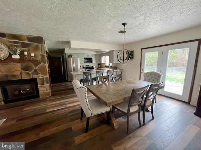 dining space with a textured ceiling, a chandelier, dark hardwood / wood-style floors, and a fireplace