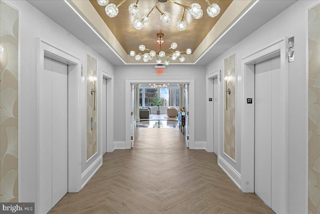 corridor with light parquet floors, a chandelier, and a raised ceiling