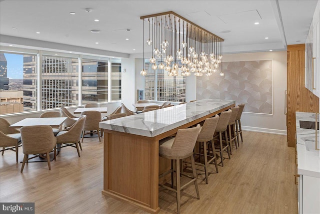 bar featuring decorative light fixtures, a notable chandelier, light hardwood / wood-style floors, white cabinets, and light stone counters