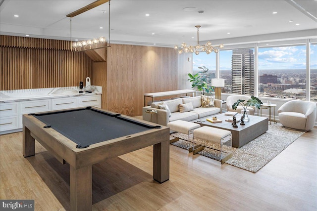 rec room with wooden walls, a notable chandelier, pool table, and light hardwood / wood-style floors