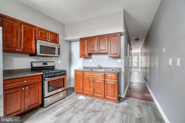 kitchen featuring appliances with stainless steel finishes, dark stone counters, sink, and light wood-type flooring