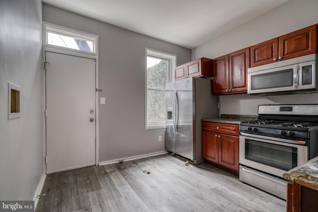 kitchen featuring dark stone countertops, appliances with stainless steel finishes, and light hardwood / wood-style flooring