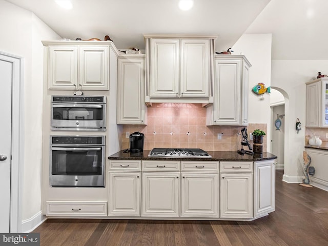 kitchen with appliances with stainless steel finishes, backsplash, dark stone countertops, and dark hardwood / wood-style flooring