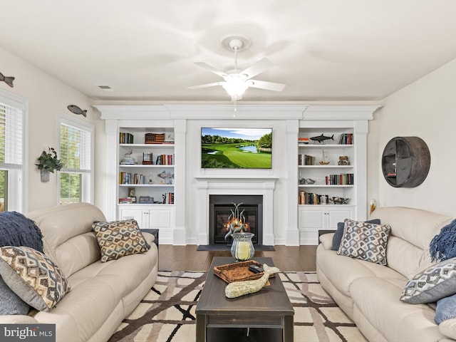 living room featuring built in shelves, ceiling fan, and wood-type flooring