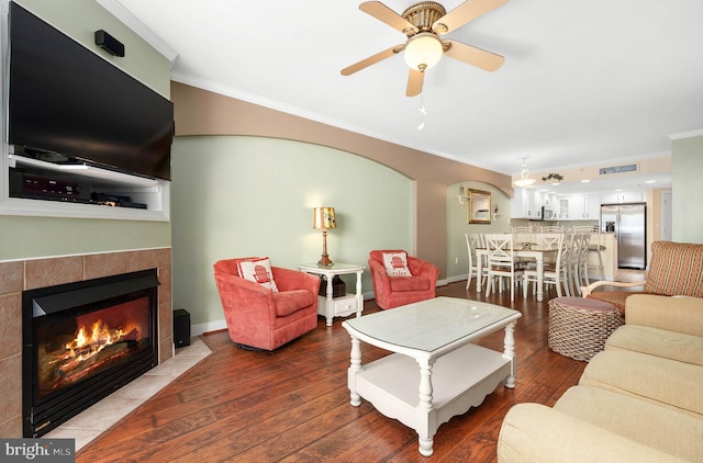 living room featuring ceiling fan, ornamental molding, a fireplace, and wood-type flooring