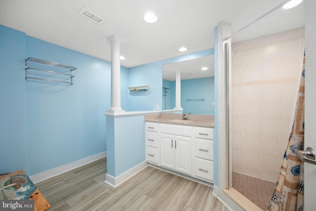 bathroom featuring hardwood / wood-style floors, large vanity, decorative columns, and tiled shower